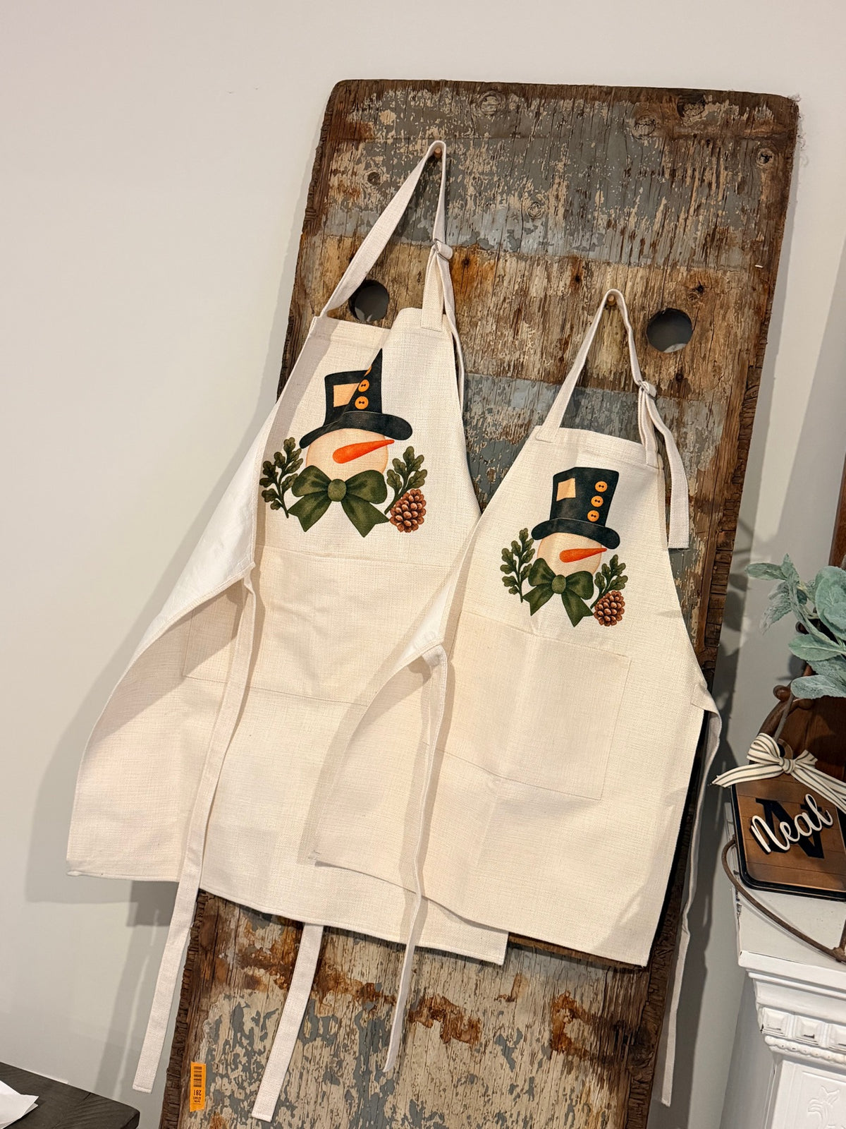 Adult and child snowman aprons hanging together, showing the sizes
