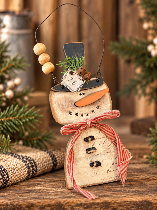 Wonky primitive square-face snowman with red ribbon in a subtle rustic setting