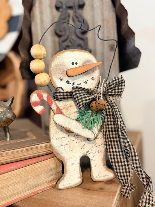 Finished primitive snowman sitter with candy cane and black check bow, front view