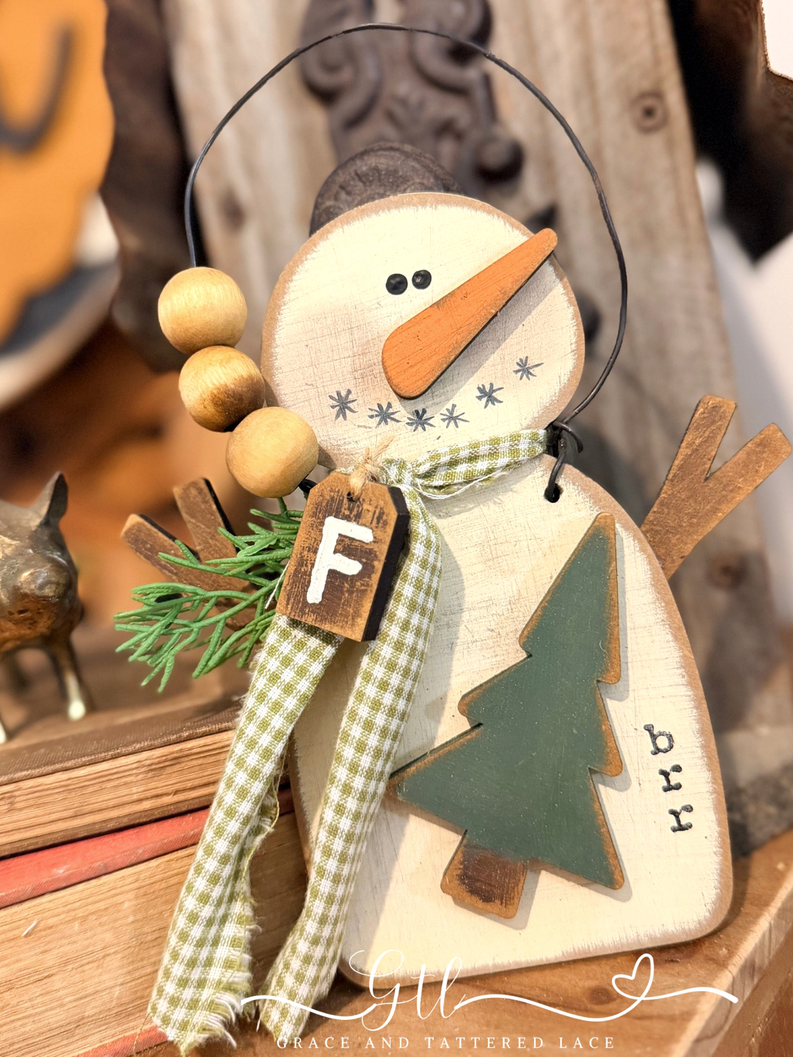 Finished rustic primitive snowman ornament with a green Christmas tree, gingham scarf, and wooden bead accents